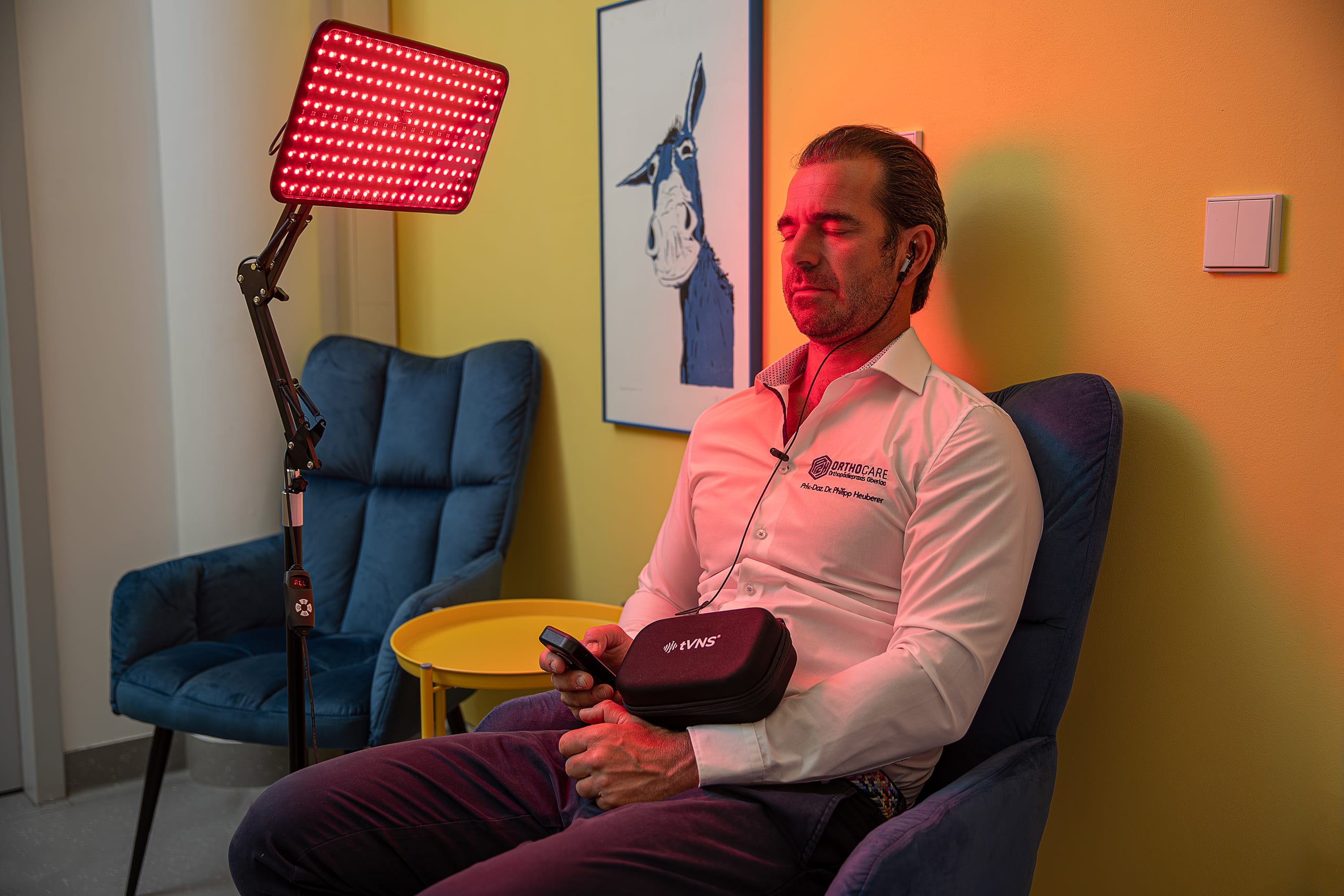 Mann sitzt mit geschlossenen Augen vor einer roten LED-Lichttherapielampe