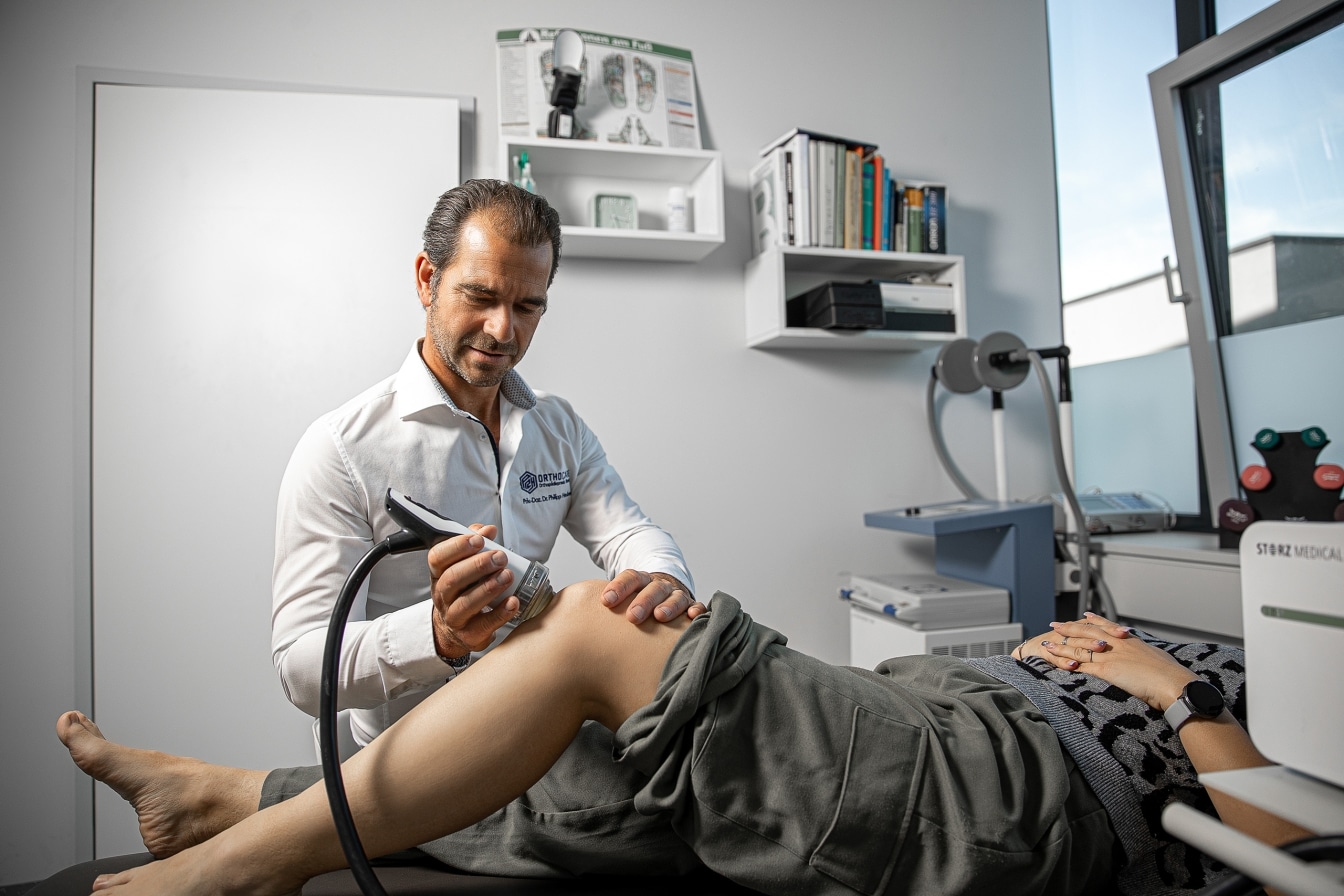 Arzt untersucht das Knie einer Patientin mit einem Ultraschallgerät in einer Praxis